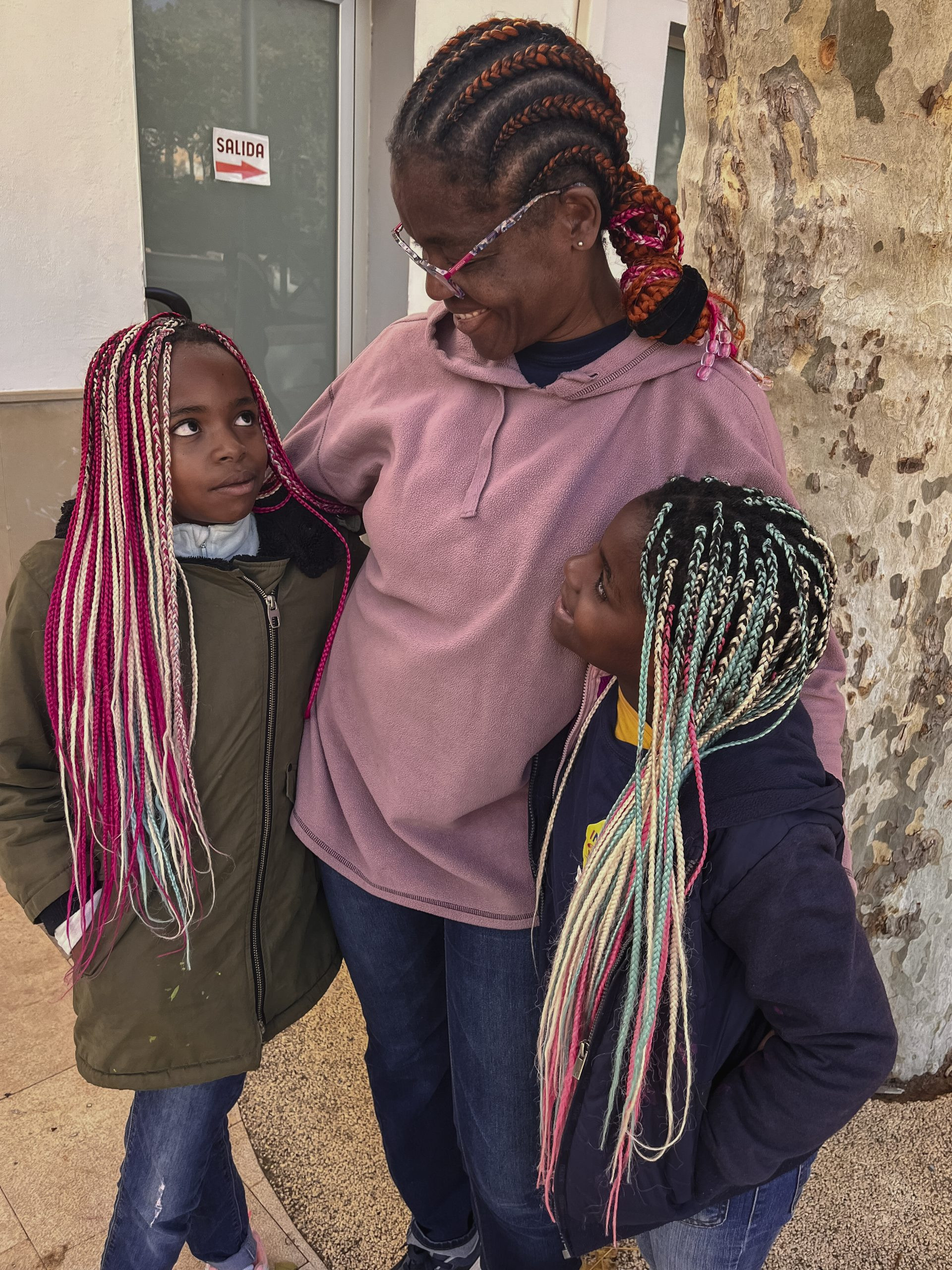 A woman and two girls hugging. All of them with colorful braided hair.