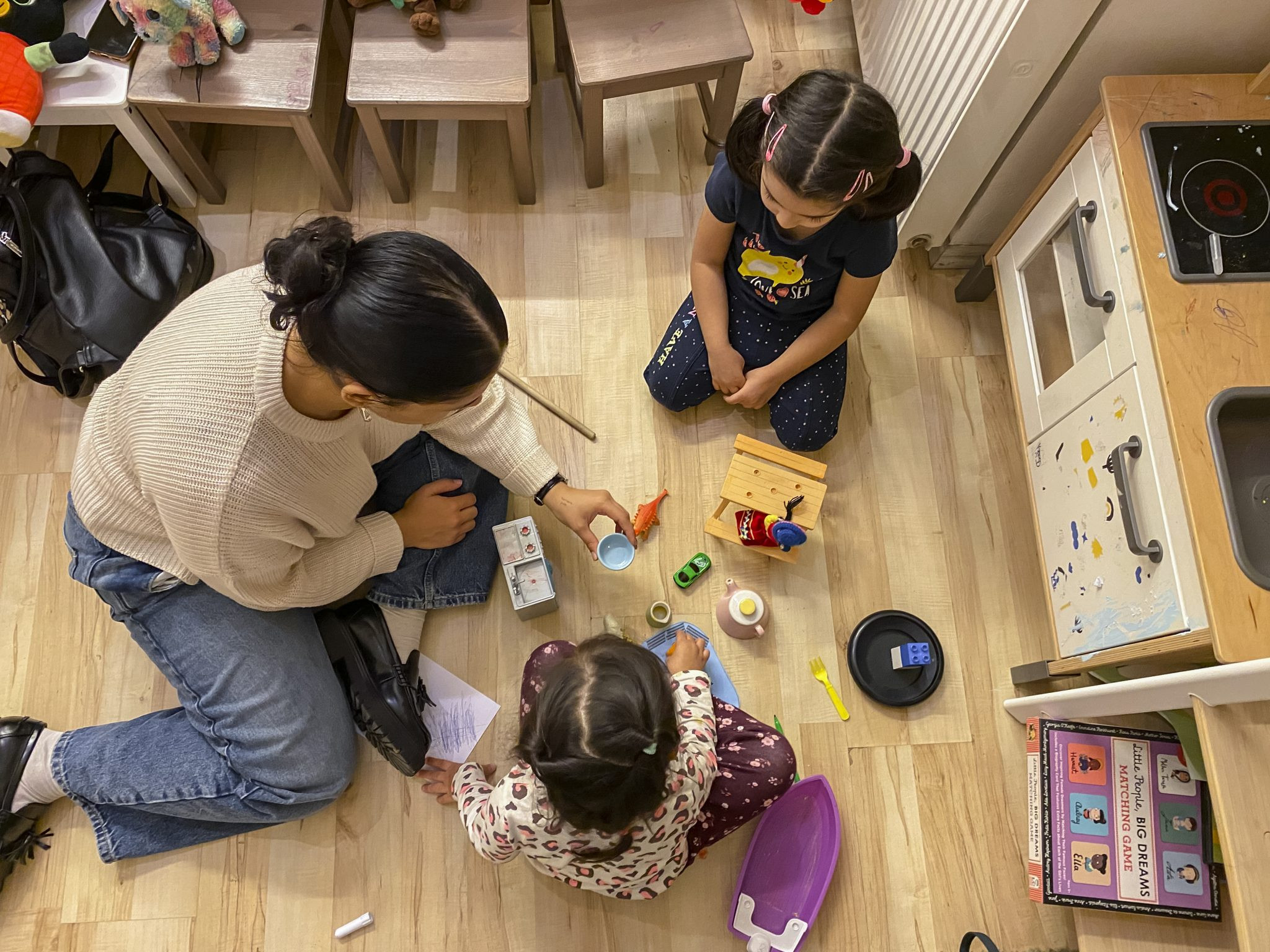 A woman and two little girls playing with toys on the floor.