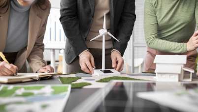 Three people's hands working on a miniature house and wind turbine